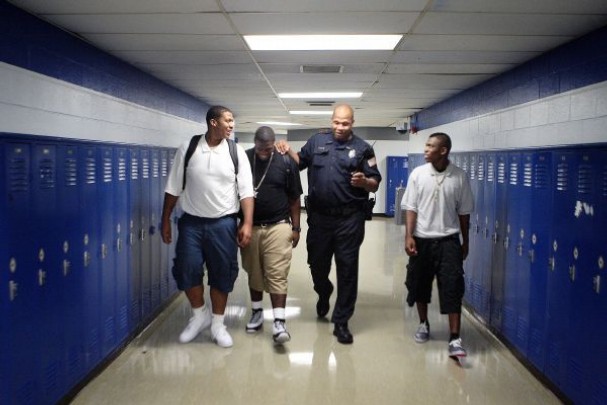 Law enforcement officer walkinng with 3 young boys of color